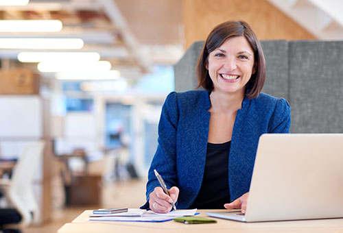 smiling woman in office setting using laptop computer