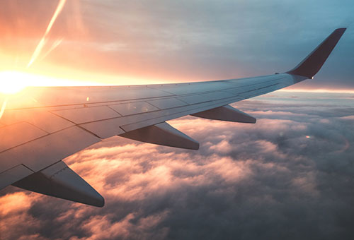 sun shining over airplane wing above the clouds