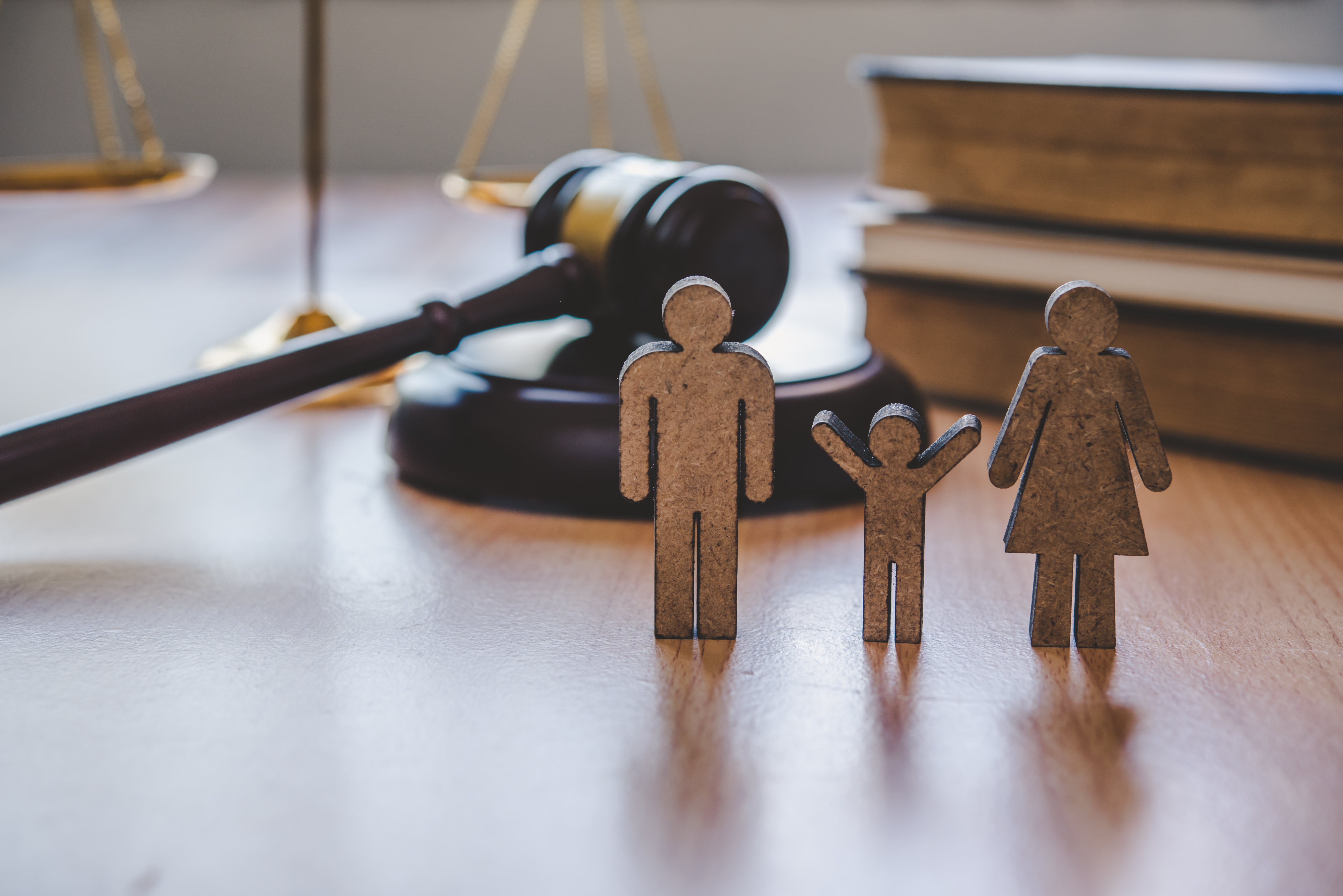 small wooden people standing on desk in front of gavel, scale and books