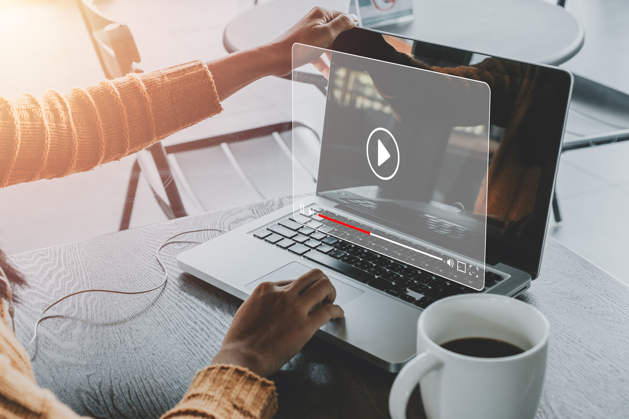 person using laptop computer with video playing and cup of coffee sitting beside laptop