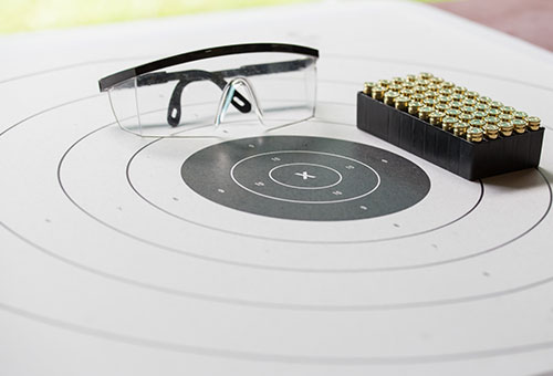 paper shooting target diagram with safety glasses and ammunition sitting on top