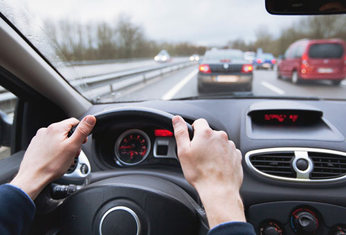 driver inside car with both hands on the steering wheel seeing traffic on highway out the windshield