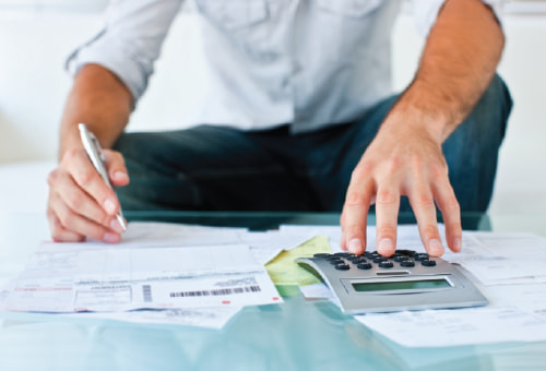 Person working at a low glass table covered with bills and a calculator